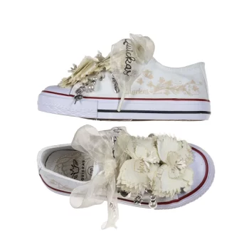 Sneaker de algodón con puntera con estampado de mariposas en los laterales de color beige suave. Realizadas a mano, lleva dos mariposas de organza y crepe en la parte superior con pasador para que se puedan quitar y volver a colocar. Los cordones son en forma de lazada de organza en color natural con detalle de laminado QUICKAS. A ambos lados lleva abalorios con acabado plateado y adorno de perlas con anillas para que puedas poner y quitar.
