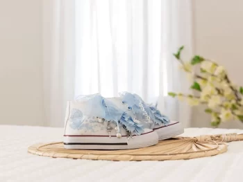 Botas de algodón con puntera con estampados de mariposas en los laterales de color cielo. Están realizadas a mano, lleva mariposas de organza y crepe en la parte superior. Los cordones son en forma de lazada de organza en color blanco con detalle de laminado QUICKAS.