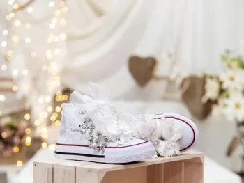 Botas de algodón con puntera con estampados de mariposas en los laterales de color gris perla. Están realizadas a mano, lleva mariposas de organza y crepe en la parte superior. Los cordones son en forma de lazada de organza en color blanco con detalle de laminado QUICKAS.