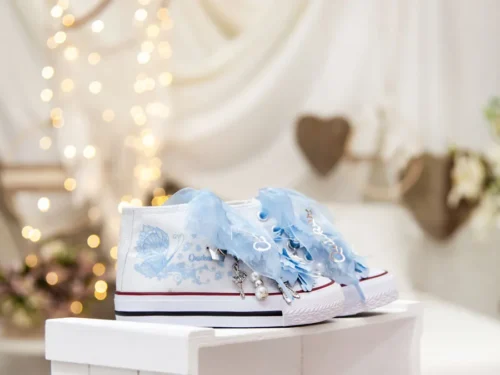Botas de algodón con puntera con estampados de mariposas en los laterales de color cielo. Están realizadas a mano, lleva mariposas de organza y crepe en la parte superior. Los cordones son en forma de lazada de organza en color blanco con detalle de laminado QUICKAS.